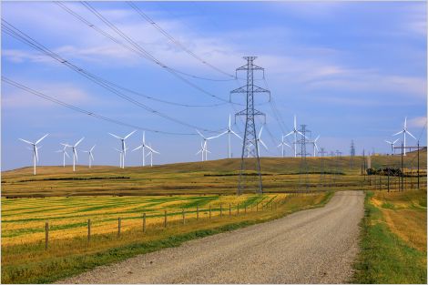 A road passing through a field with wind turbines and transmission lines