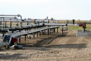 A well site in Alberta, in a rural setting with fields in the background