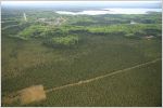 Aerial view of well pad (square, clear-cut area) with road access in the midst of the boreal forest; lake and clear sky in background