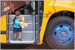 Small child with stuffed animals exiting electric school bus