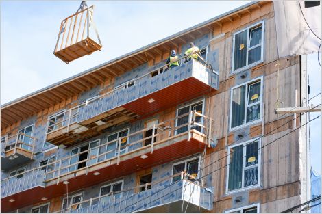 Two construction crew members standing on scaffolding against third story of a building being retrofitted