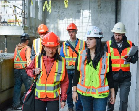 Women in construction helmets and high-visibility vests at a green building construction site.