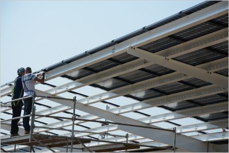 Two people installing solar modules on a large framework
