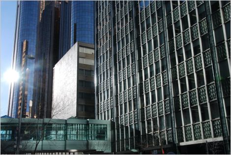 A corporate headquarters in Calgary towers over a bustling downtown metropolis, surrounded by a mix of skyscrapers and tower blocks in an urban outdoor setting.