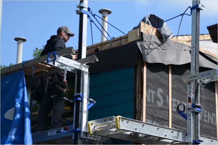 Worker on scaffolding retrofitting multifamily house