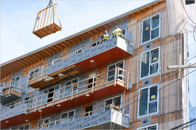 Two construction crew members standing on scaffolding against third story of a building being retrofitted