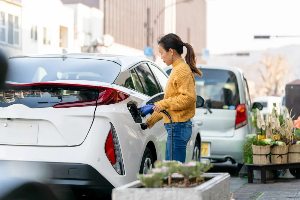 a woman is plugging in a white electric vehicle