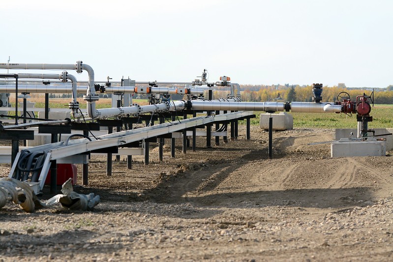 A well site in Alberta, in a rural setting with fields in the background