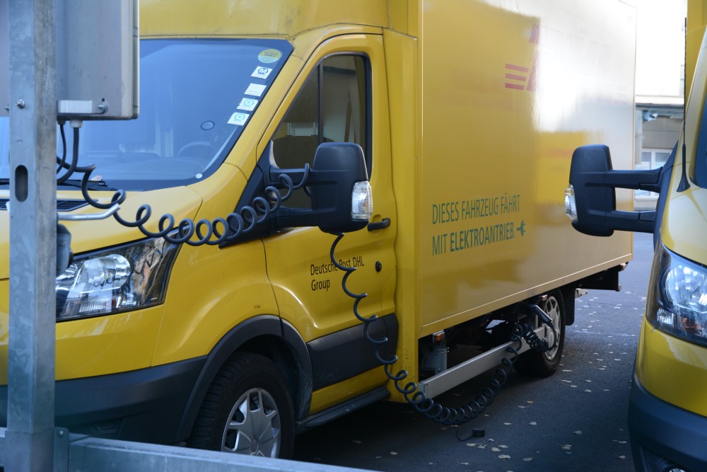 Electric delivery truck charging at a station with the charger positioned in front of the vehicle