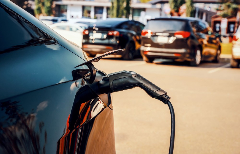 Black electric car at charging station with the power cable supply plugged in