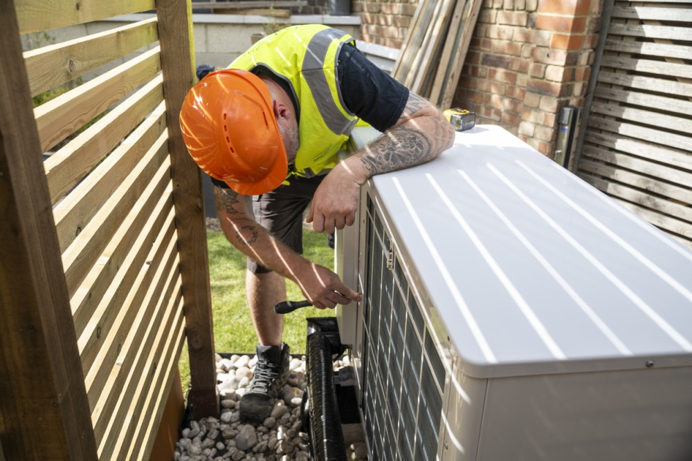 Electrician installing a heat pump in a garden on a sunny day