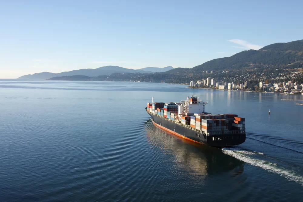 A container ship setting sail from a port with blue skies in the background