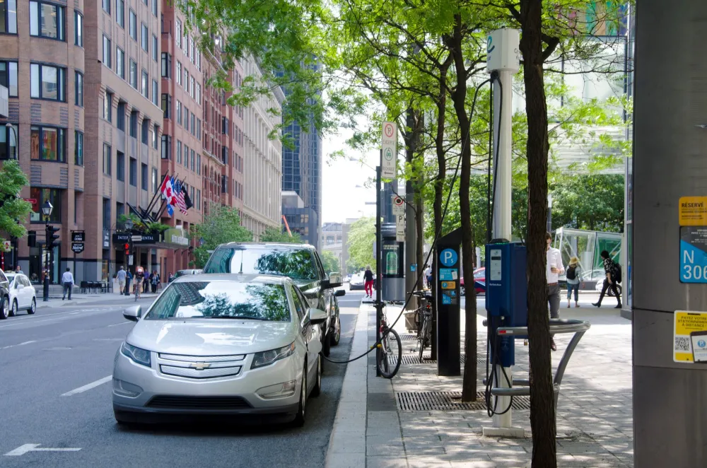  Electric car charging at recharging station in the street under green trees in summertime