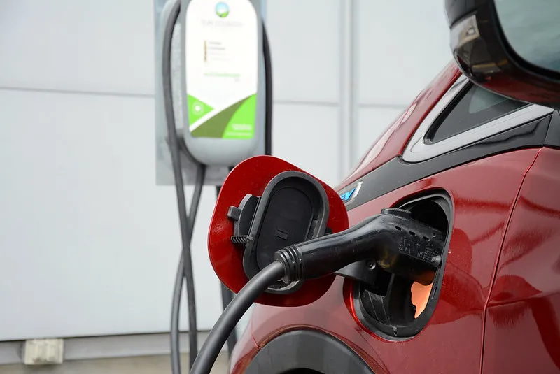 Close-up of a red electric vehicle charging, with a charging cable plugged into the car's port
