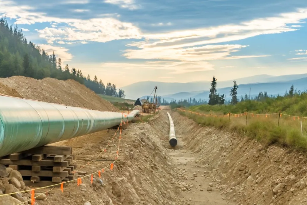 A picture of a pipeline under construction, with mountains and forest in the background