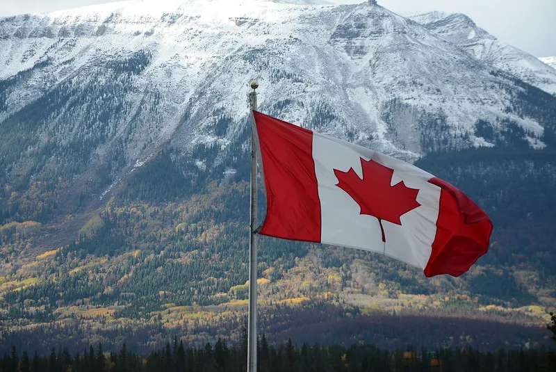A Canadian flag flying in front of a snow covered mountain