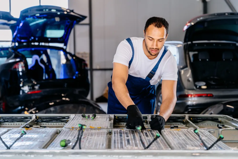 An electric vehicle technician servicing a battery with two EVs parked behind him