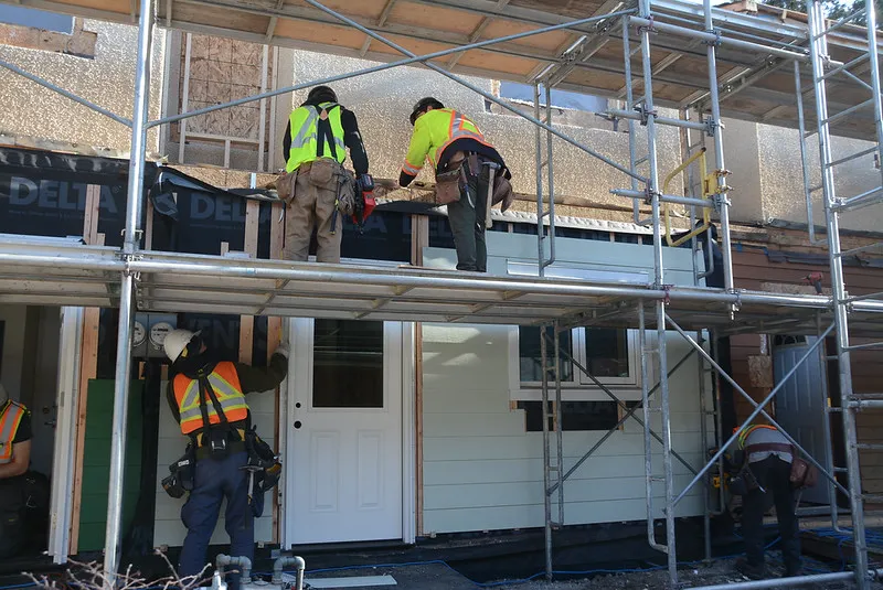 Workers in safety vests on scaffolding retrofitting a home unit