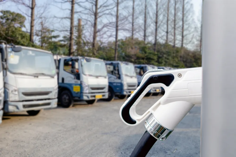 Close-up of an electric vehicle charging plug with trucks in the background