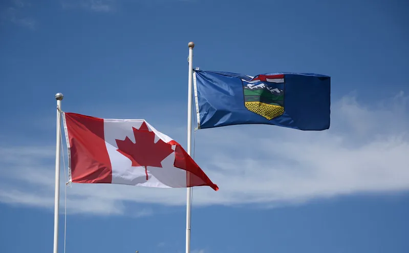 The flags of Canada and Alberta against a blue sky with clouds