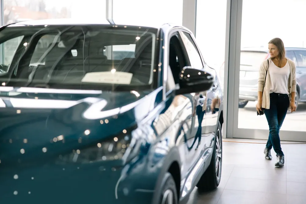 Woman walking around a car at a dealership, looking closely at its features