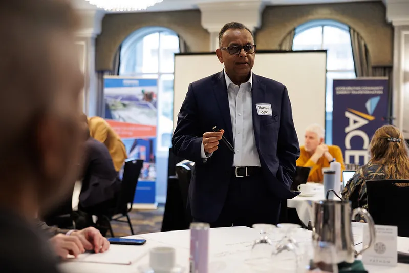 Male workshop participant standing at a table during the Pembina Institute and ACET Sustainable Jobs in BC workshop, speaking to colleagues as they discuss the topic. Pembina and ACET banners are visible in the background of the workshop room.
