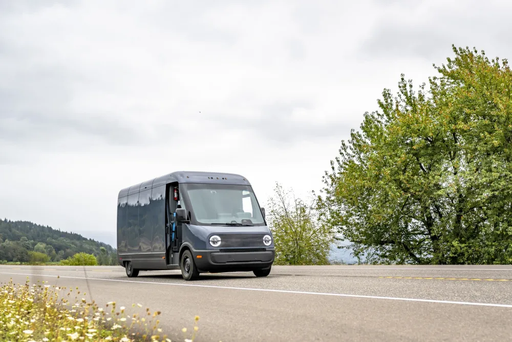 Electric cargo mini van driving on a road driving through a green, tree-lined area