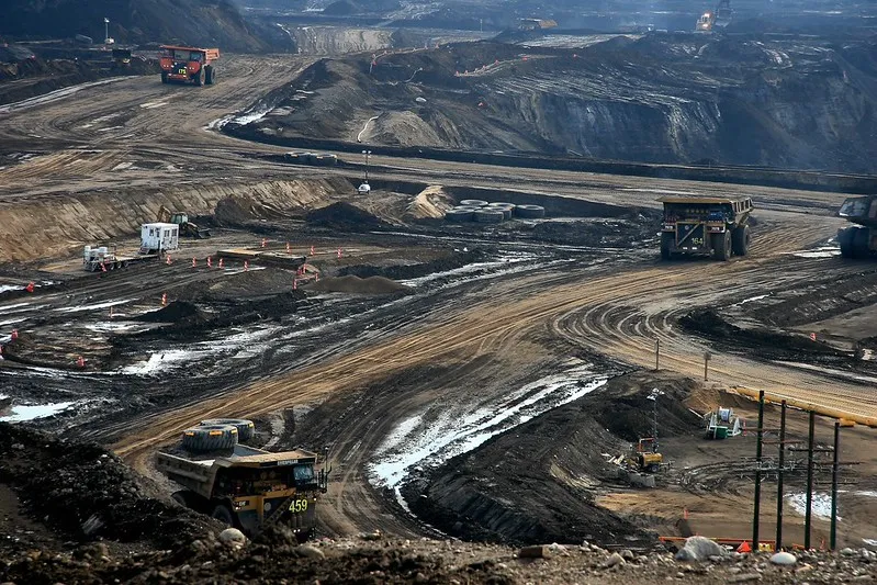 An oilsands mine in Alberta with three trucks driving through