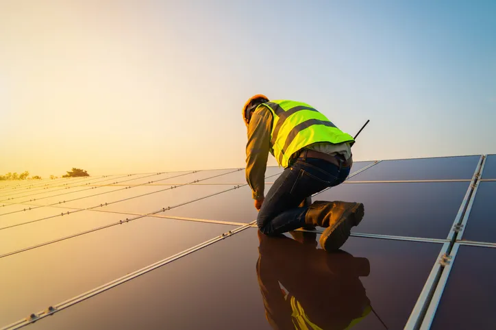 Person installing rooftop solar panels at sunset