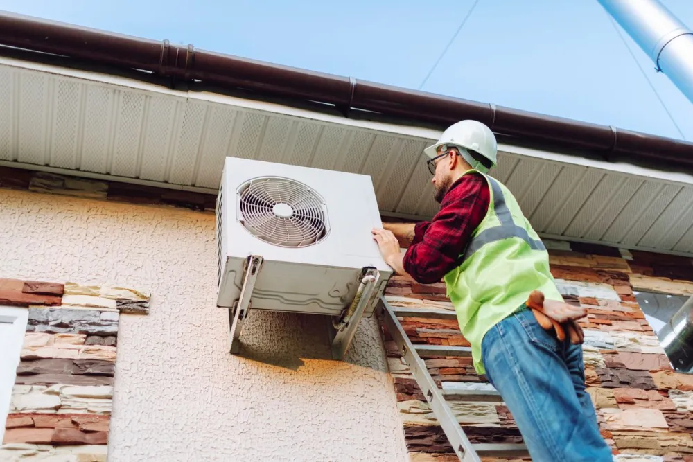 Worker installs air conditioning unit on a house