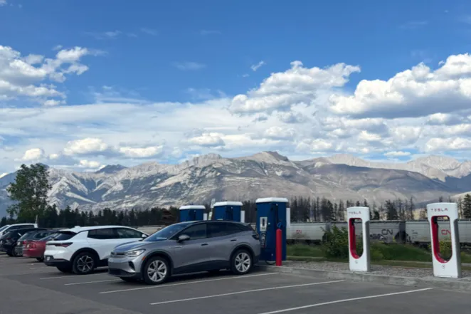 A Volkswagen ID.4 charging at Tesla Superchargers in Jasper, Alberta, with Rocky Mountains in the background.
