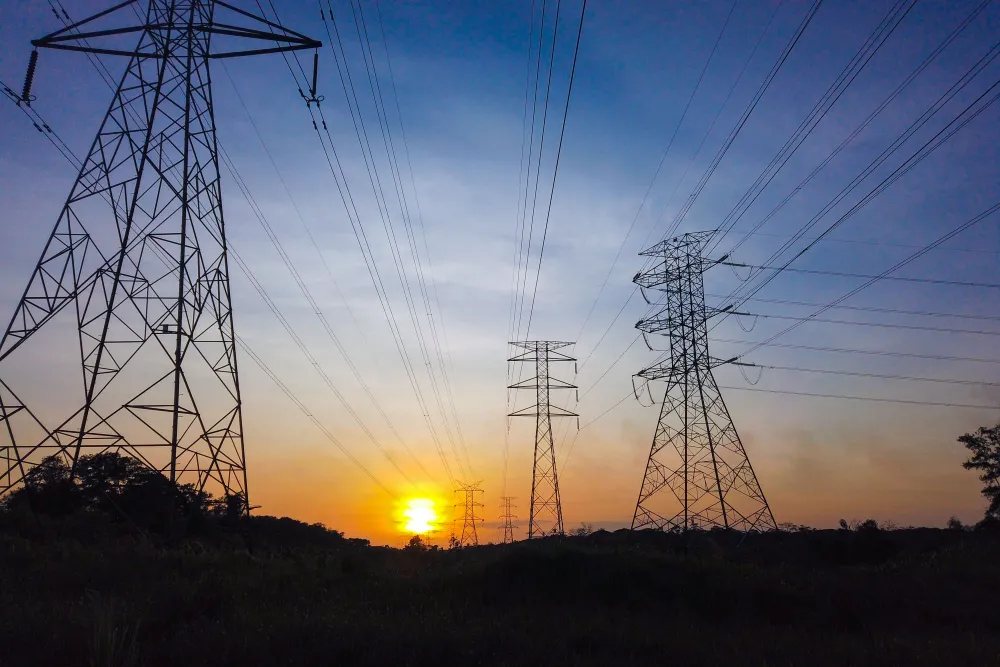 Silhouetted power lines and towers against a striking sunset sky, illustrating energy supply themes.