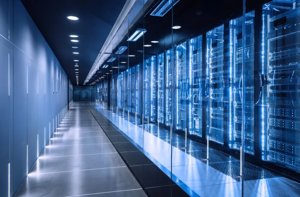 A horizontal, wide shot of a futuristic data center corridor with rows of server racks and control panels, illuminated by a cool blue glow and overhead lighting, creating a sense of depth and complexity in a symmetrical composition.