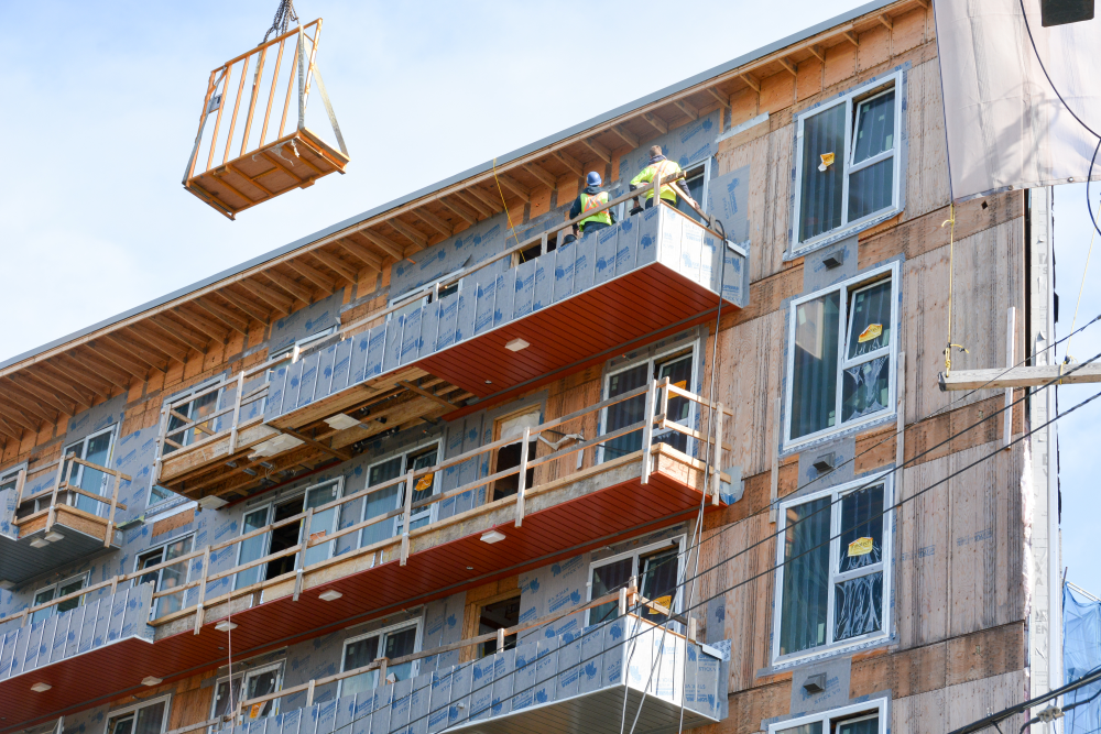 Two construction crew members standing on scaffolding against third story of a building being retrofitted