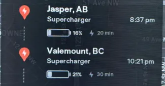 Close-up of a Tesla display showing battery levels and charging information at different locations.