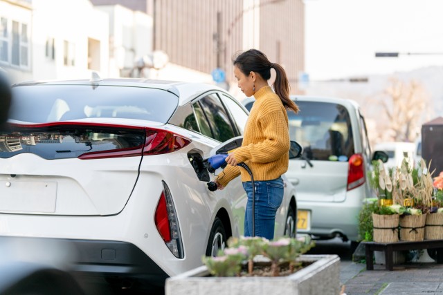 a woman is plugging in a white electric vehicle
