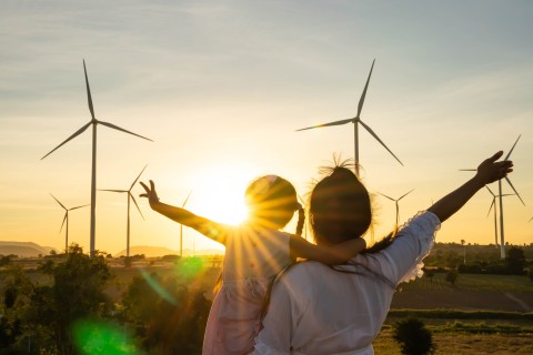 Parent and child in front of wind turbines at sunset