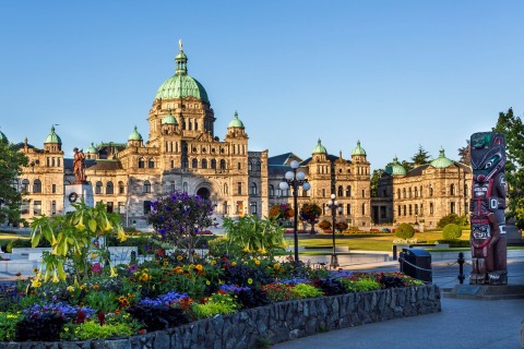 British Columbia parliament building in Victoria, B.C., with flower gardens and a nearby totem pole