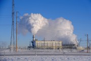 An electricity plant in winter with snow on the ground. There is steam coming out of the power station chimney