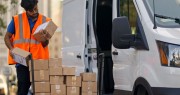 Delivery person beside white van, inspecting a package