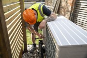 Electrician installing a heat pump in a garden on a sunny day