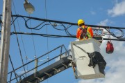 Utility worker in safety gear repairing power lines from a bucket lift under a clear blue sky