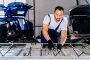 An electric vehicle technician servicing a battery with two EVs parked behind him