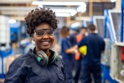 Female employee in protective workwear at a solar panel factory, looking at the camera smiling
