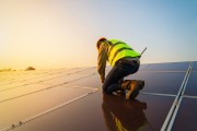 Person installing rooftop solar panels at sunset