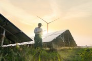 Construction worker standing in front of solar panels and wind turbine