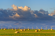 Windmills in the distance in front of mountain views and behind a field of haybales 